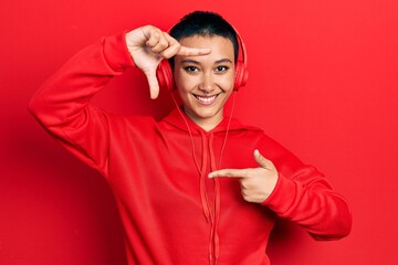 Beautiful hispanic woman with short hair listening to music using headphones smiling making frame with hands and fingers with happy face. creativity and photography concept.