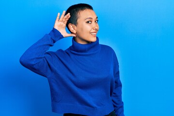 Beautiful hispanic woman with short hair wearing turtleneck sweater smiling with hand over ear listening an hearing to rumor or gossip. deafness concept.