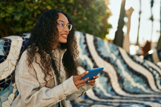 Young latin woman smiling happy using touchpad sitting on the bench at the city.