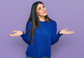 Young hispanic woman wearing casual clothes clueless and confused expression with arms and hands...