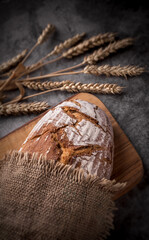 Wholegrain fresh baked rustic crust bread with rye stalks in jute bag on wooden board and gray marble kitchen table ready to eat arrangement