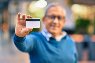 Senior grey-haired man smiling happy holding credit card at the city.