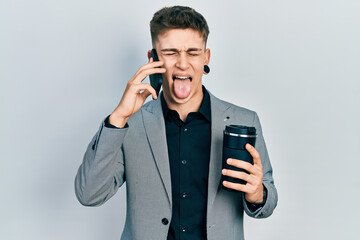 Young caucasian boy with ears dilation using smartphone and drinking a cup of coffee sticking tongue out happy with funny expression.
