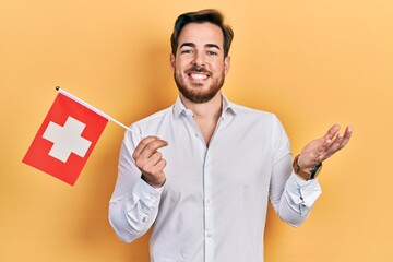 Handsome caucasian man with beard holding switzerland flag celebrating achievement with happy smile...