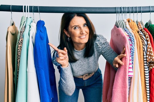 Middle age brunette woman working as professional personal shopper smiling happy pointing with hand and finger to the side