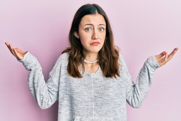 Young brunette woman wearing casual sweater clueless and confused with open arms, no idea and...