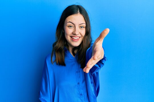 Young brunette woman wearing casual blue shirt smiling friendly offering handshake as greeting and welcoming. successful business.