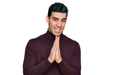 Handsome hispanic man wearing casual turtleneck sweater praying with hands together asking for forgiveness smiling confident.