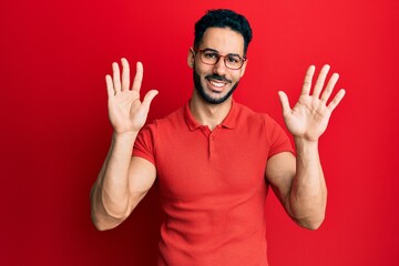Naklejka premium Young hispanic man wearing casual clothes and glasses showing and pointing up with fingers number ten while smiling confident and happy.