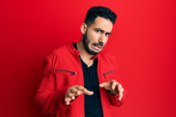 Young hispanic man wearing red leather jacket disgusted expression, displeased and fearful doing disgust face because aversion reaction.