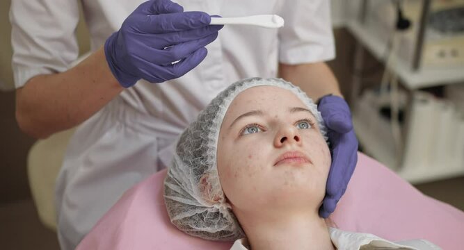 Applying Peeling on the face. A young girl in a cosmetology office is undergoing facial skin rejuvenation procedures. Cosmetology. Girl beautician works with patients in the office