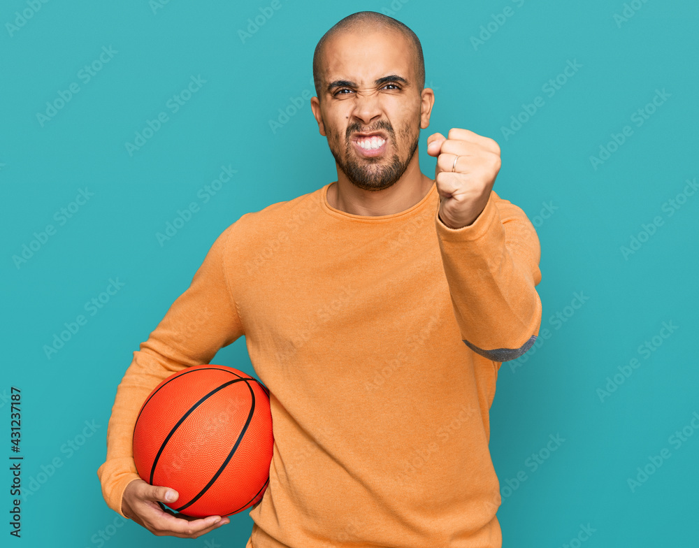 Sticker hispanic adult man holding basketball ball annoyed and frustrated shouting with anger, yelling crazy