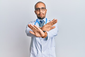 Hispanic adult man wearing doctor uniform and stethoscope rejection expression crossing arms doing negative sign, angry face