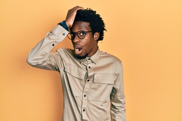 Young african american man wearing casual clothes and glasses surprised with hand on head for mistake, remember error. forgot, bad memory concept.