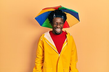 Young african american man wearing yellow raincoat winking looking at the camera with sexy...