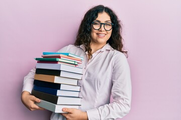 Young brunette woman with curly hair holding a pile of books smiling and laughing hard out loud because funny crazy joke.