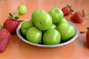 background of green plums in a plate and strawberries on the table