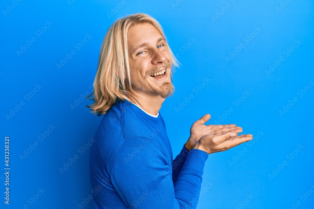 Sticker Caucasian young man with long hair presenting with open palms, holding something smiling and laughing hard out loud because funny crazy joke.