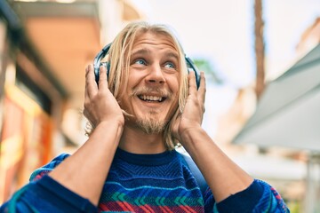 Young scandinavian student man smiling happy using headphones at the city.