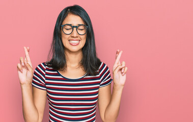 Beautiful asian young woman wearing casual clothes and glasses gesturing finger crossed smiling with hope and eyes closed. luck and superstitious concept.