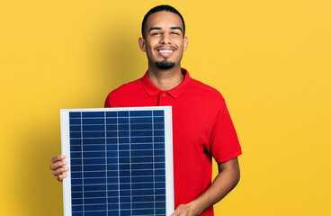 Young african american man holding photovoltaic solar panel smiling with a happy and cool smile on face. showing teeth.