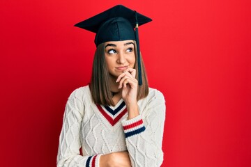 Young brunette girl wearing graduation cap serious face thinking about question with hand on chin, thoughtful about confusing idea