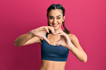 Young brunette girl wearing sportswear and braids smiling in love doing heart symbol shape with...