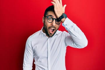 Young hispanic businessman wearing shirt and glasses surprised with hand on head for mistake,...