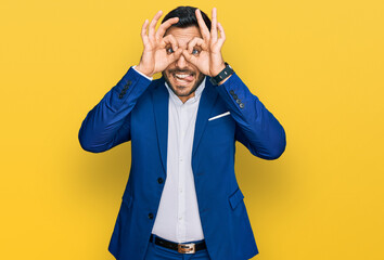 Young hispanic man wearing business jacket doing ok gesture like binoculars sticking tongue out, eyes looking through fingers. crazy expression.