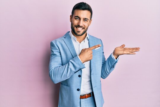 Young hispanic businessman wearing business jacket amazed and smiling to the camera while presenting with hand and pointing with finger.