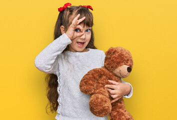 Little caucasian girl kid hugging teddy bear stuffed animal smiling happy doing ok sign with hand...