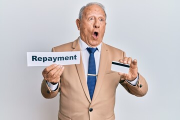 Senior caucasian man holding payment word paper and credit card in shock face, looking skeptical...
