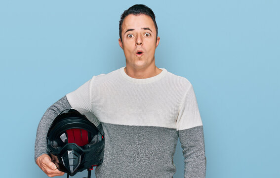Handsome young man holding motorcycle helmet scared and amazed with open mouth for surprise, disbelief face