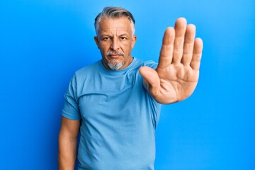 Middle age grey-haired man wearing casual clothes doing stop sing with palm of the hand. warning expression with negative and serious gesture on the face.