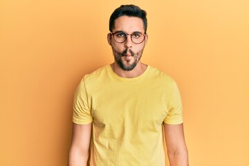 Fototapeta premium Young hispanic man wearing casual clothes and glasses making fish face with lips, crazy and comical gesture. funny expression.