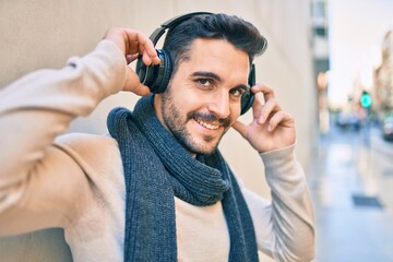 Young hispanic man smiling happy listening to music using headphones at the city.