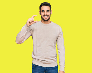 Young hispanic man wearing casual clothes smiling and confident gesturing with hand doing small size sign with fingers looking and the camera. measure concept.