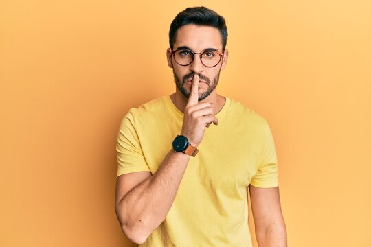 Young hispanic man wearing casual clothes and glasses asking to be quiet with finger on lips. silence and secret concept.