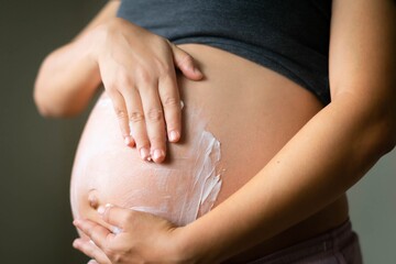 A pregnant woman massaging lotion on her baby belly. Prenatal skin care.