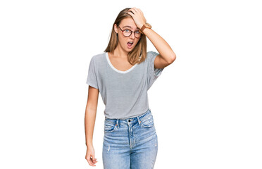 Beautiful young blonde woman wearing casual clothes and glasses surprised with hand on head for...