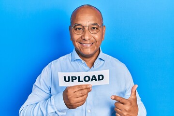Middle age latin man holding upload paper message smiling happy pointing with hand and finger