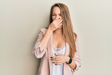 Young blonde woman wearing business jacket and glasses smelling something stinky and disgusting, intolerable smell, holding breath with fingers on nose. bad smell