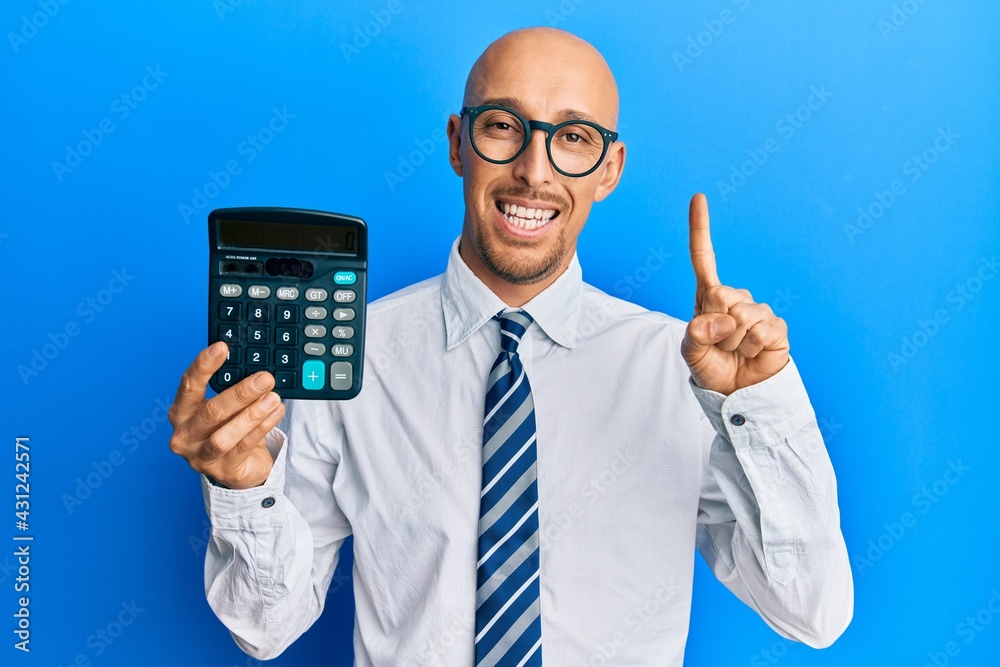 Wall mural bald business man with beard showing calculator device smiling with an idea or question pointing fin