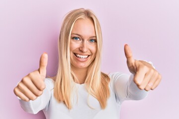 Young blonde girl wearing casual clothes approving doing positive gesture with hand, thumbs up smiling and happy for success. winner gesture.
