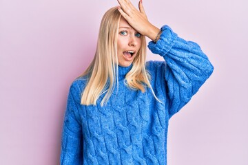 Young blonde girl wearing wool winter sweater surprised with hand on head for mistake, remember error. forgot, bad memory concept.