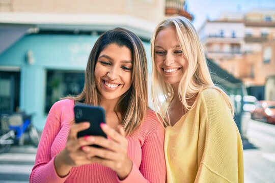 Two beautiful and young girl friends together having fun at the city using smartphone