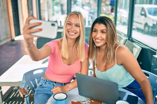 Two beautiful and young girl friends meeting at cafeteria taking a selfie picture with smartphone