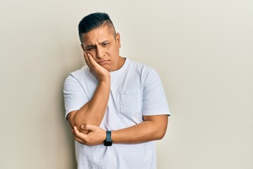 Young latin man wearing casual white t shirt thinking looking tired and bored with depression problems with crossed arms.