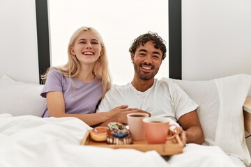 Obraz na płótnie Canvas Young beautiful couple smiling happy having breakfast on the bed at home.