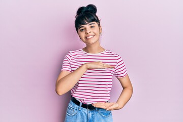 Young hispanic girl wearing casual clothes gesturing with hands showing big and large size sign, measure symbol. smiling looking at the camera. measuring concept.